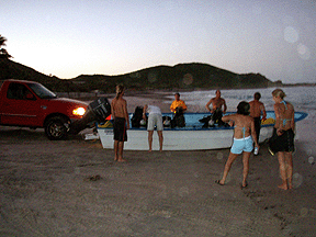 Launching panga boat from shore at night.
